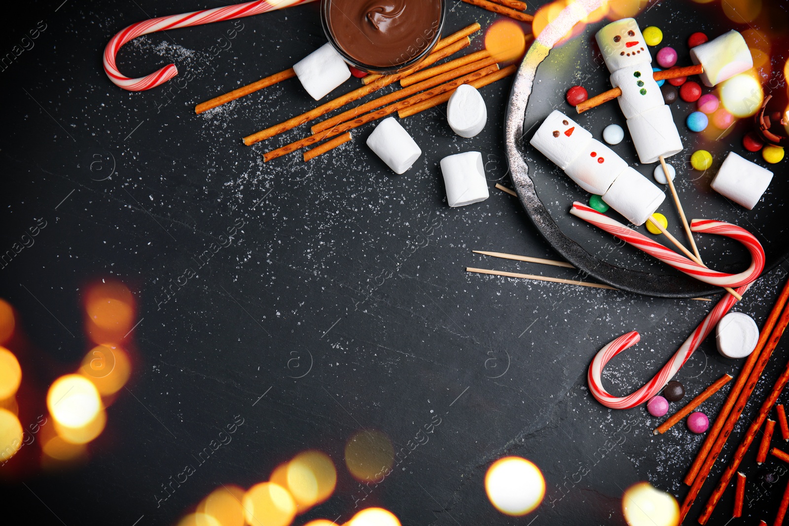 Image of Flat lay composition with funny snowmen made of marshmallows on black table, space for text. Bokeh effect