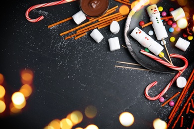 Image of Flat lay composition with funny snowmen made of marshmallows on black table, space for text. Bokeh effect