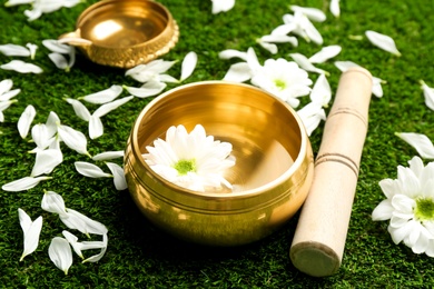 Photo of Golden singing bowl with flower and mallet on green grass, closeup. Sound healing