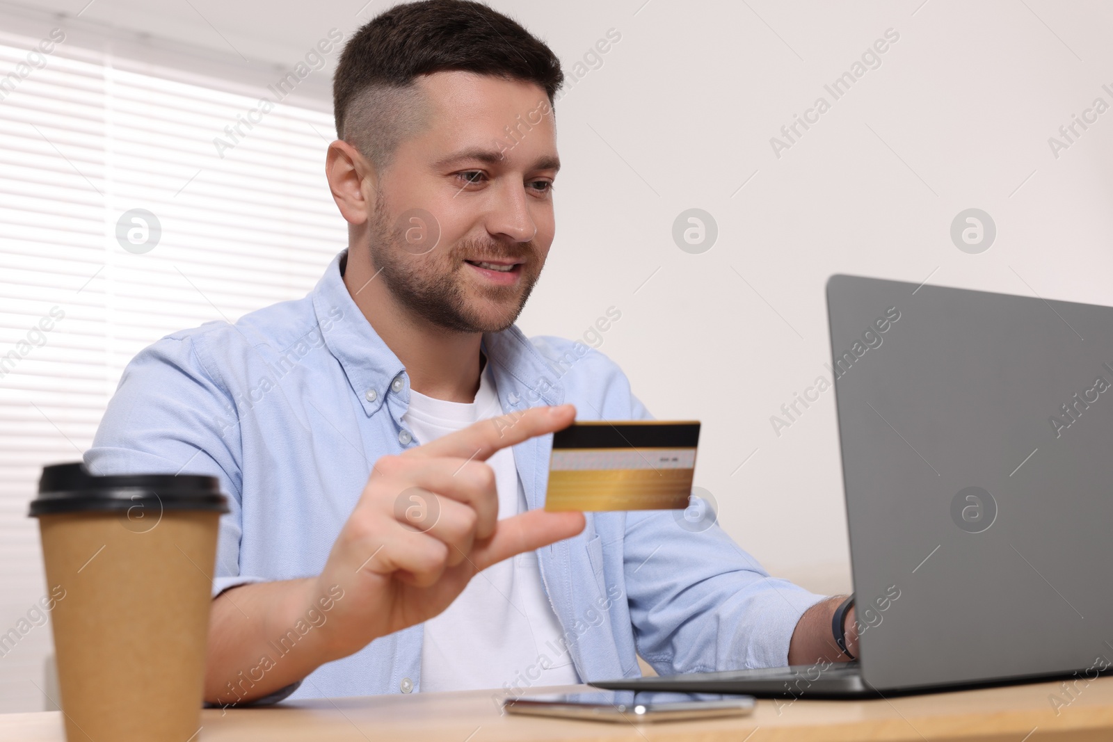 Photo of Handsome man with credit card using laptop for online shopping at table indoors