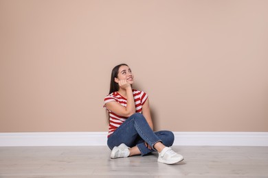 Young woman sitting on floor near beige wall indoors