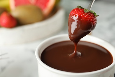 Photo of Dipping strawberry into fondue pot with chocolate, closeup. Space for text