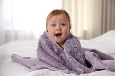 Photo of Cute little baby with soft purple towel on bed after bath