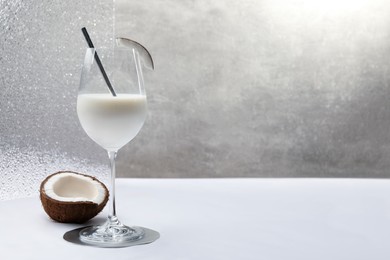 Glass of delicious coconut milk and coconut on white table, space for text
