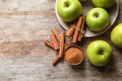 Fresh apples with cinnamon sticks and powder on wooden table, top view