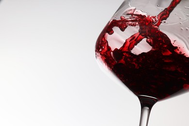 Pouring tasty red wine in glass on white background, closeup. Space for text