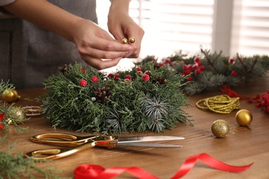 Photo of Florist making beautiful Christmas wreath at wooden table indoors, closeup