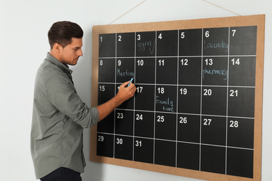 Photo of Handsome man writing with chalk on board calendar