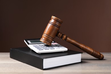 Law. Book, gavel and calculator on wooden table against brown background