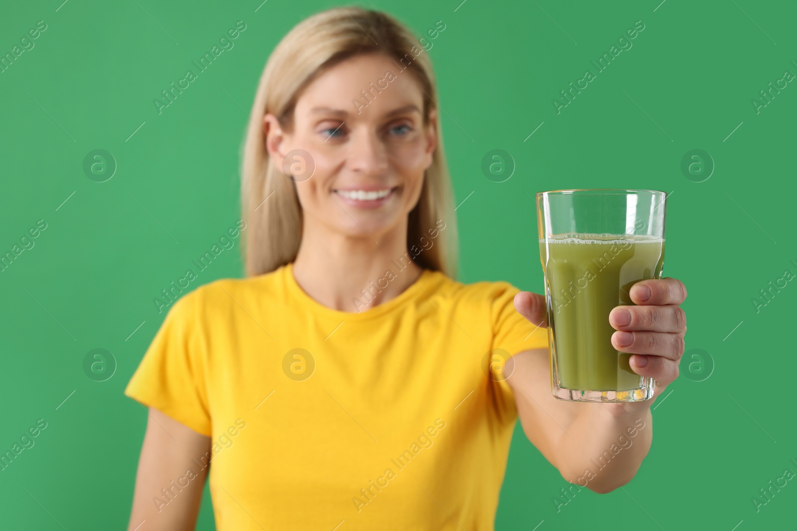 Photo of Woman with glass of tasty celery juice on green background, selective focus