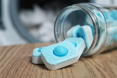 Photo of Jar with water softener tablets on wooden table near washing machine, closeup