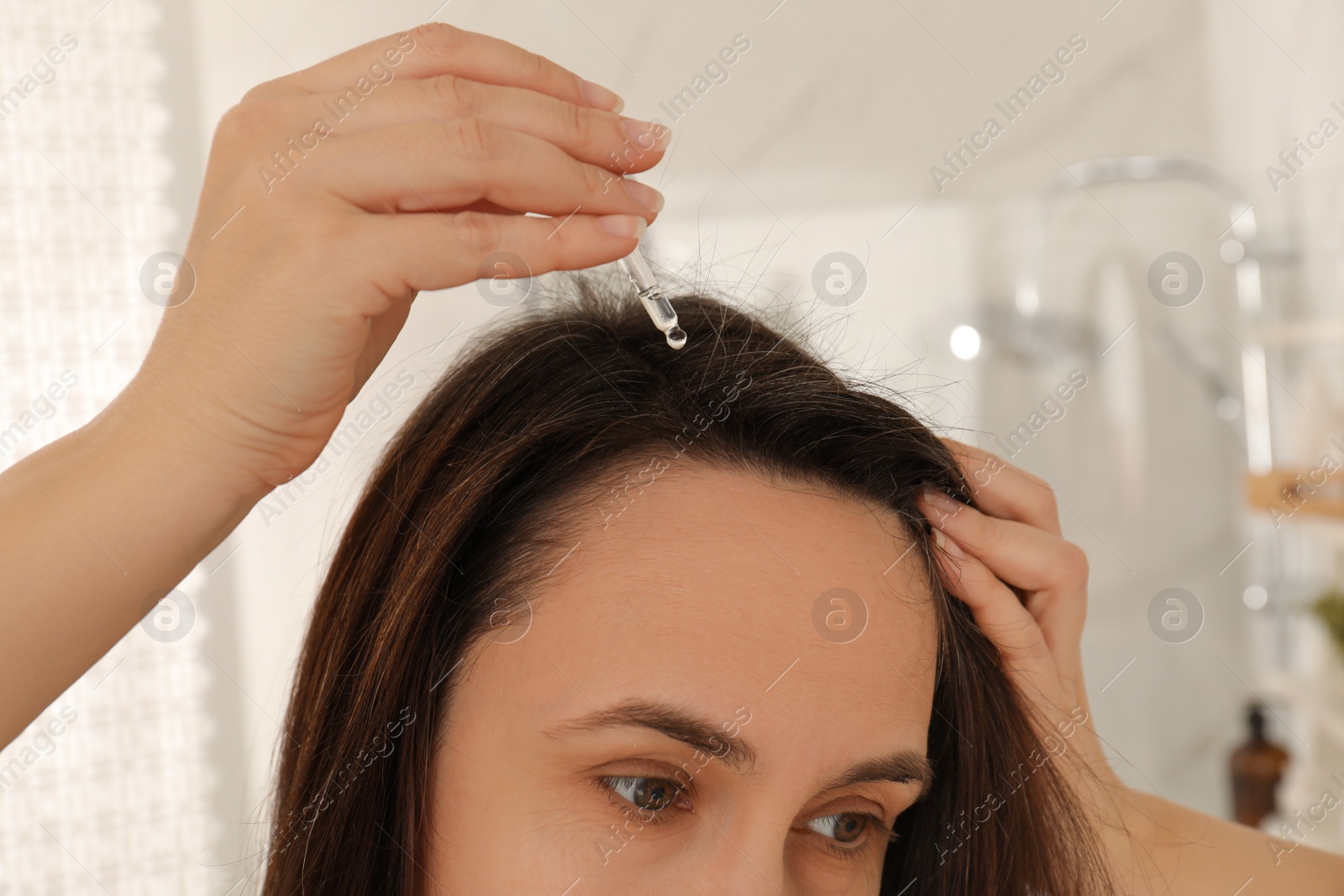 Photo of Mature woman applying oil onto hair at home, closeup. Baldness problem