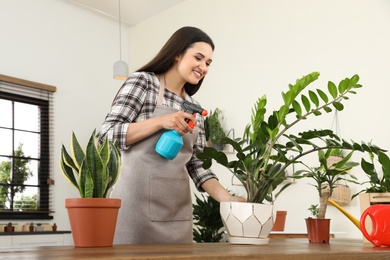 Young woman spraying plant with water at home