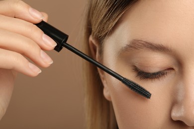 Photo of Woman applying mascara onto eyelashes against light brown background, closeup