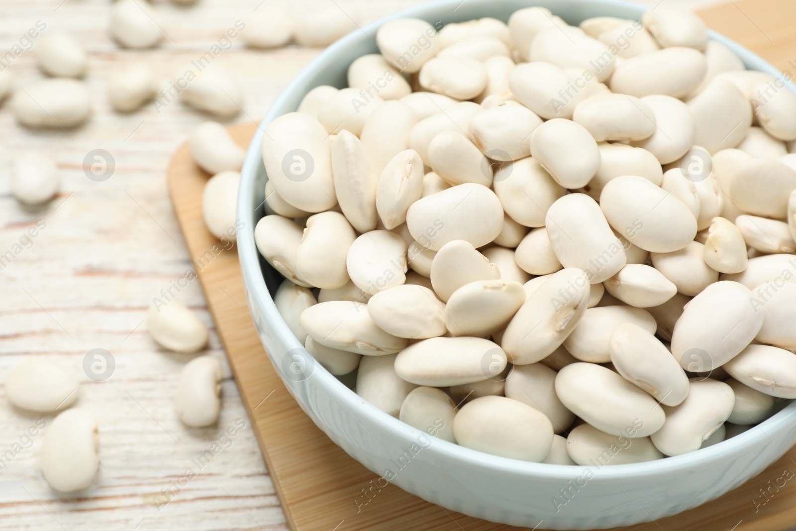 Photo of Bowl with uncooked white beans on wooden table, closeup