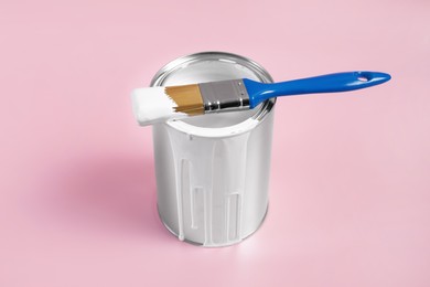 Photo of Can of white paint and brush on pink background