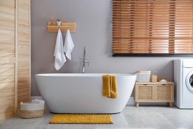 Photo of Soft orange mat on floor near tub in bathroom. Interior design