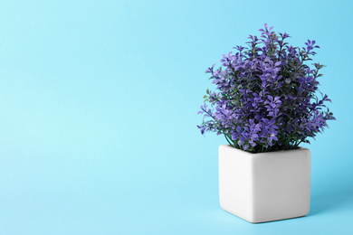 Beautiful artificial plant in flower pot on light blue background, space for text