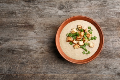 Bowl of fresh homemade mushroom soup on wooden background, top view with space for text