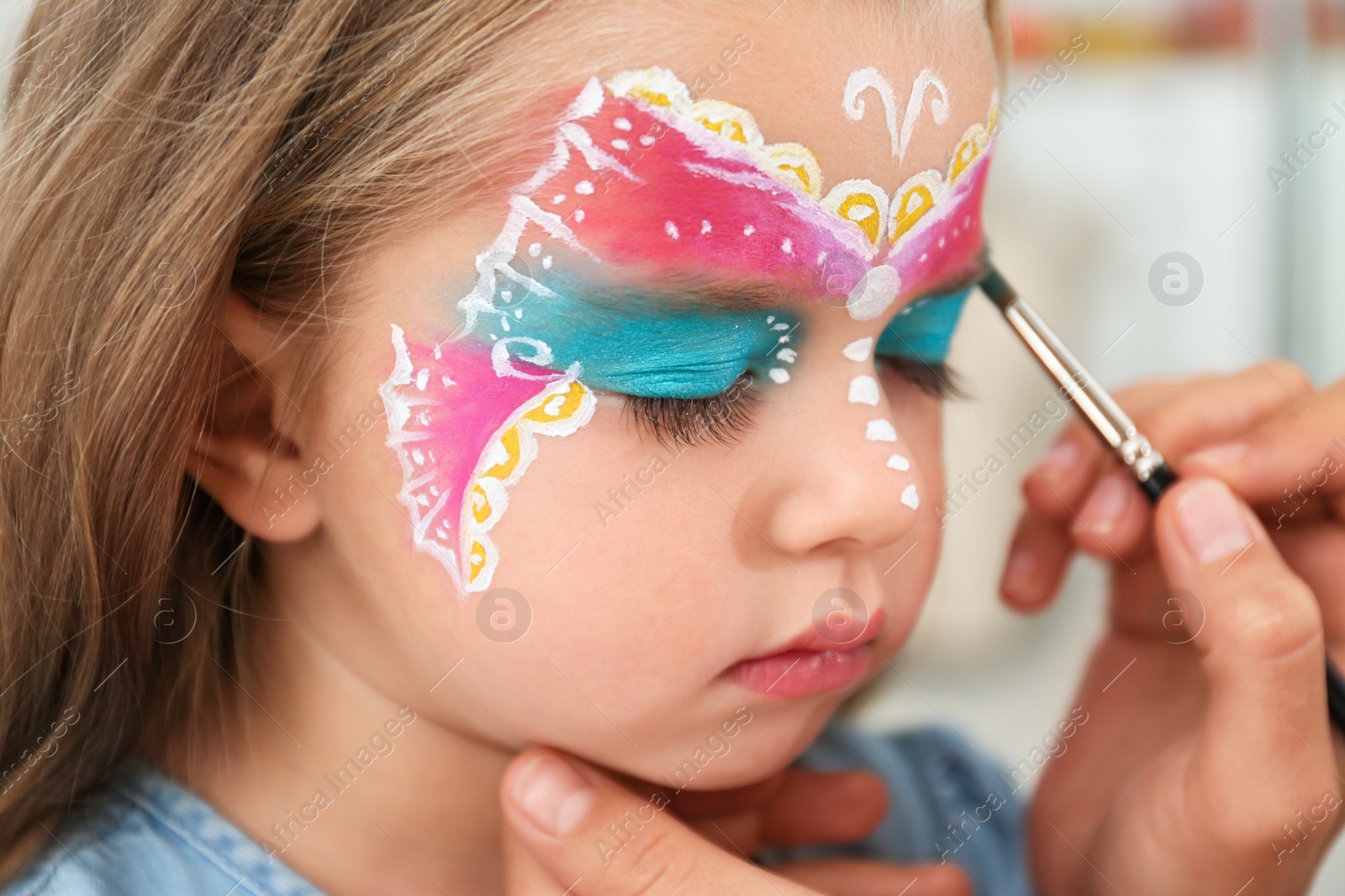 Photo of Artist painting face of little girl indoors, closeup