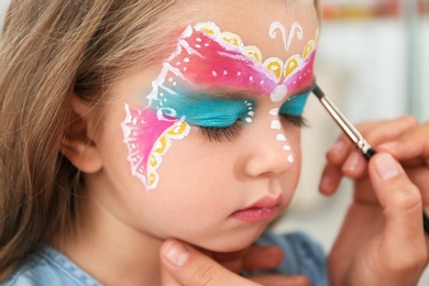 Photo of Artist painting face of little girl indoors, closeup