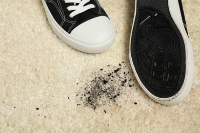 Photo of Black sneakers and mud on beige carpet, top view