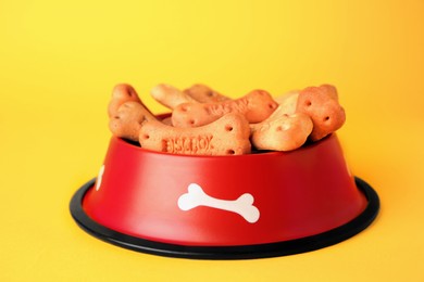 Bone shaped dog cookies in feeding bowl on yellow background