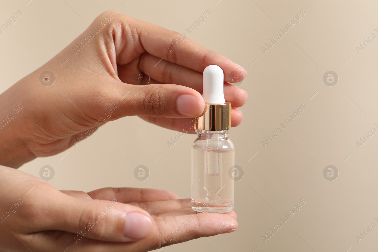 Photo of Woman with bottle of cosmetic serum on beige background, closeup