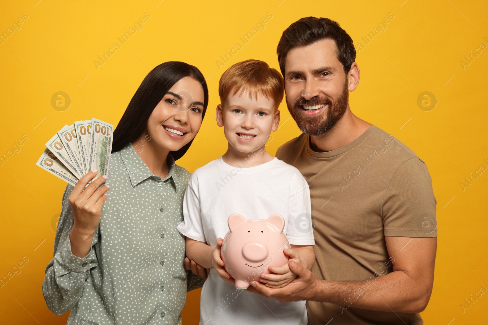 Photo of Happy family with ceramic piggy bank and money on orange background