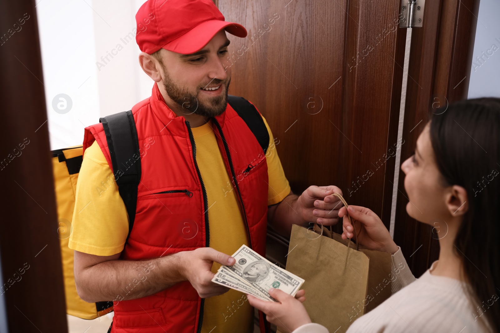 Photo of Young woman giving tips to deliveryman indoors