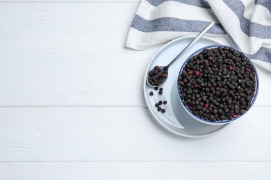 Photo of Bowl and spoon with dried blueberries on white wooden table, top view. Space for text