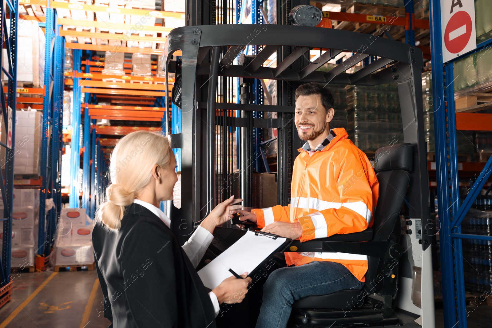 Photo of Happy worker talking with manager while sitting in forklift truck at warehouse