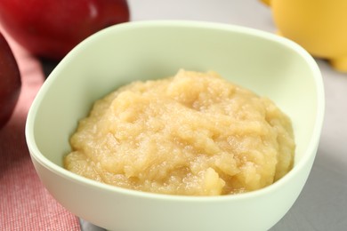 Healthy baby food. Bowl with delicious apple puree on light grey table, closeup