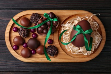 Photo of Tasty chocolate eggs with green bows and sweets on wooden table, top view