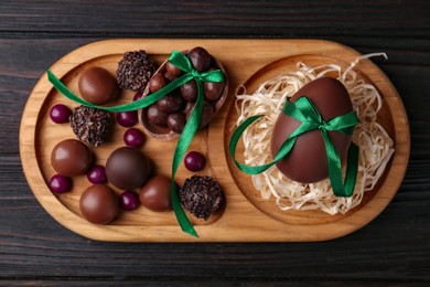 Tasty chocolate eggs with green bows and sweets on wooden table, top view