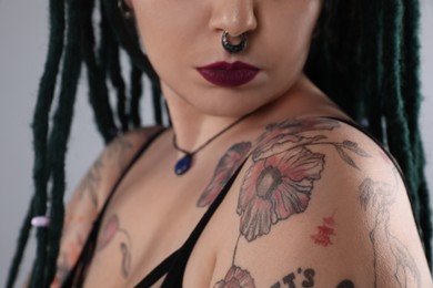 Photo of Young woman with tattoos on body, nose piercing and dreadlocks against grey background, closeup