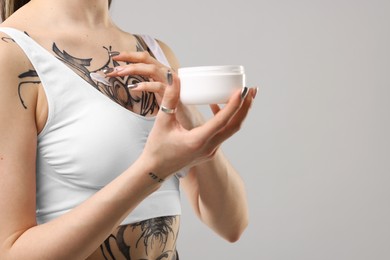 Woman applying healing cream onto her tattoos against grey background, closeup. Space for text