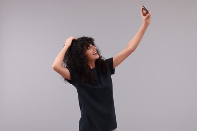 Beautiful young woman taking selfie on light grey background