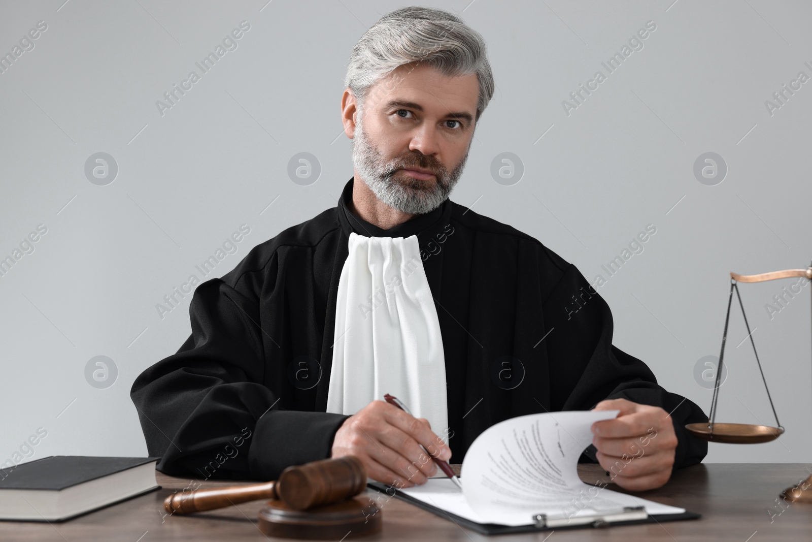 Photo of Judge with gavel and papers sitting at wooden table against light grey background