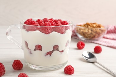 Tasty yogurt served with raspberries and muesli on white wooden table