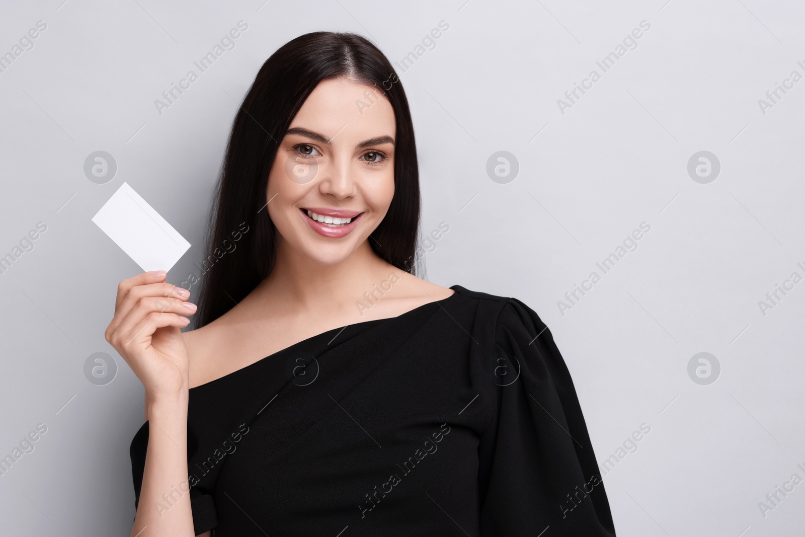 Photo of Happy woman holding blank business card on light grey background. Space for text