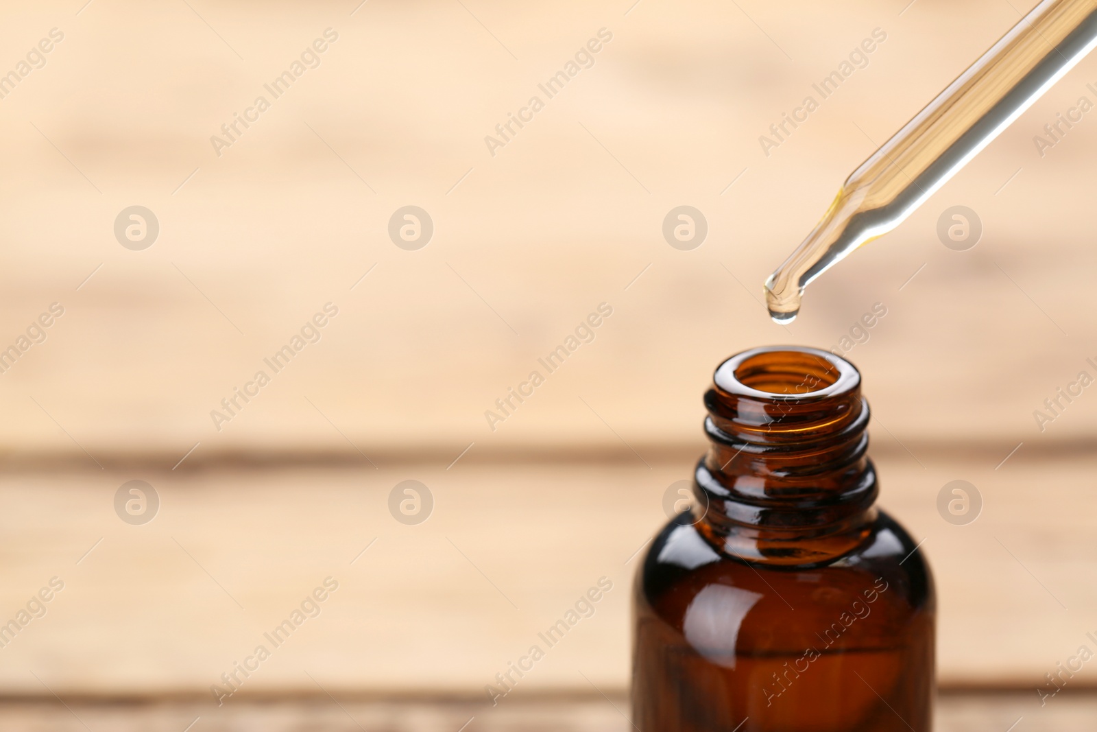 Photo of Dripping essential oil into glass bottle on wooden background, closeup. Space for text