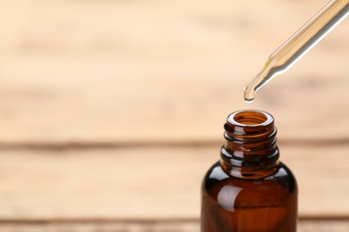 Photo of Dripping essential oil into glass bottle on wooden background, closeup. Space for text