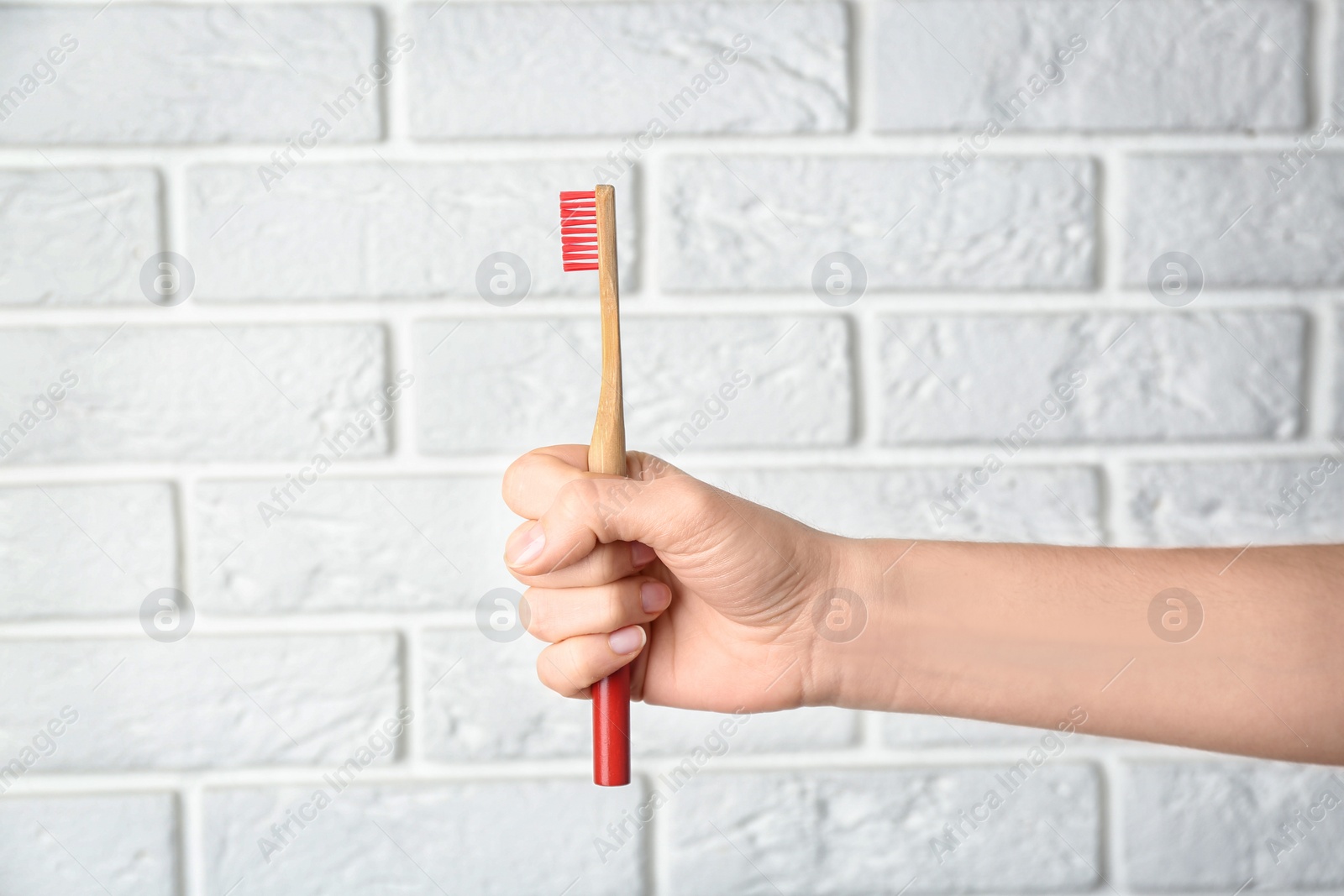 Photo of Woman holding bamboo toothbrush against white brick wall, closeup