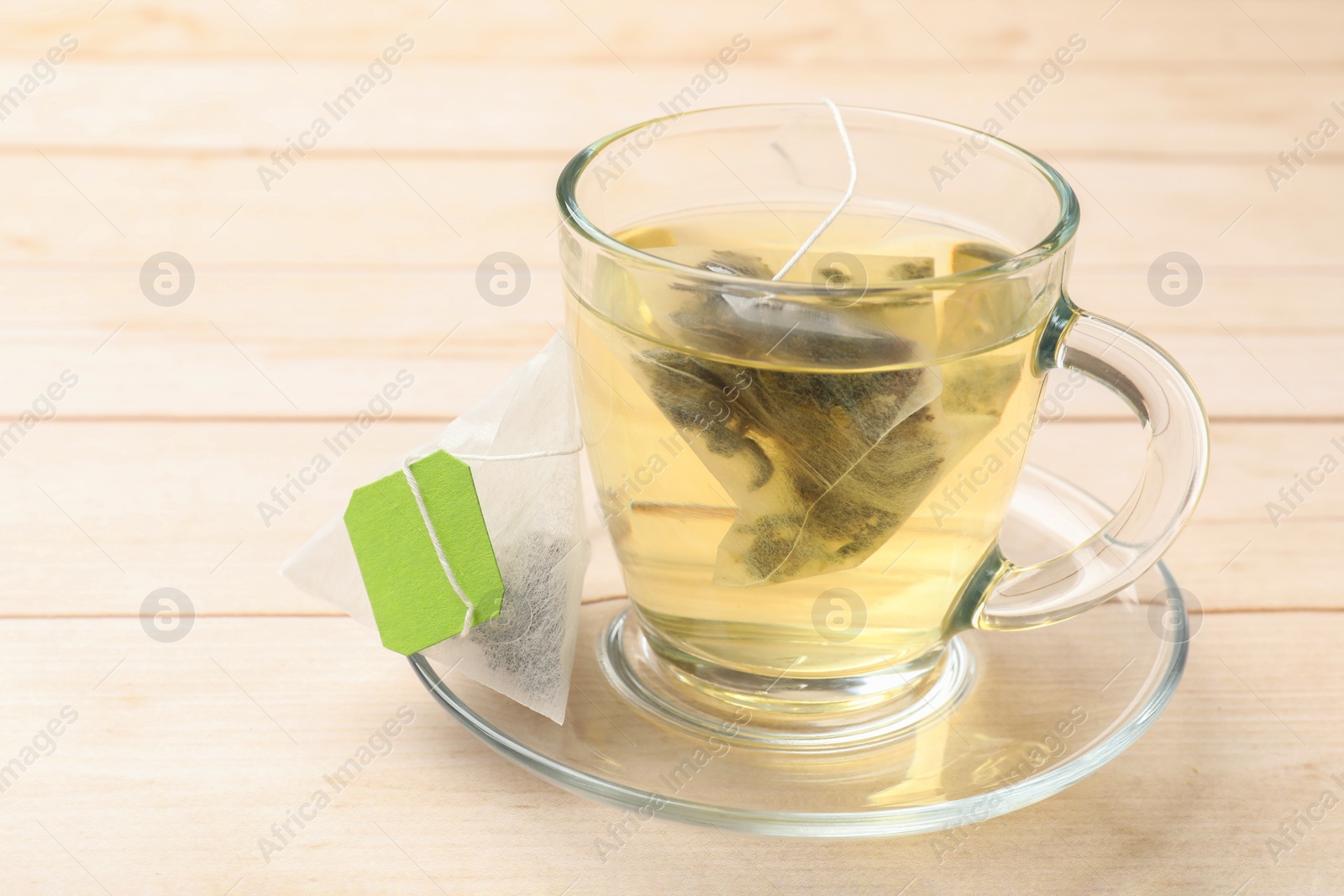Photo of Tea bag in glass cup on light wooden table, closeup