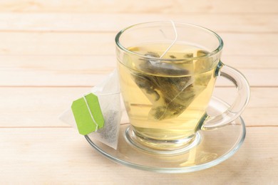 Tea bag in glass cup on light wooden table, closeup