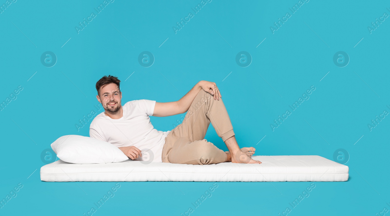 Photo of Man lying on soft mattress against light blue background