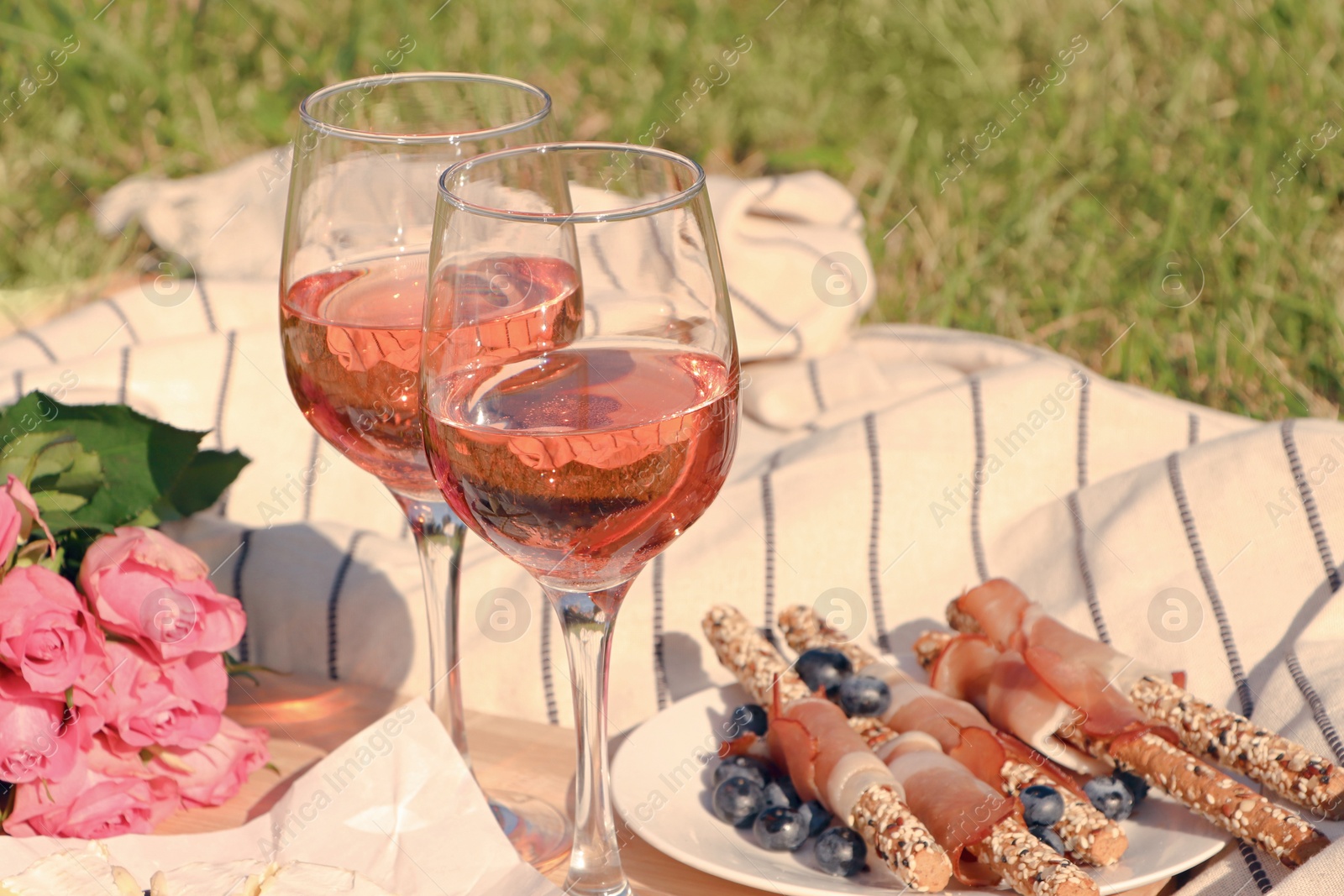 Photo of Glasses of delicious rose wine, flowers and food on picnic blanket outdoors