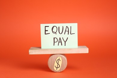 Photo of Equal pay concept. Paper note on miniature seesaw against red background