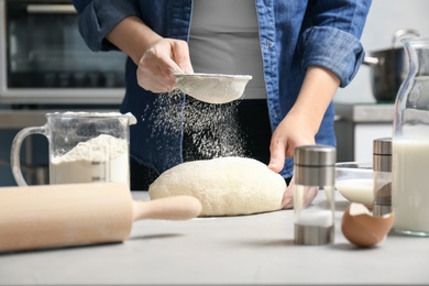 Woman sprinkling flour over dough on table in kitchen